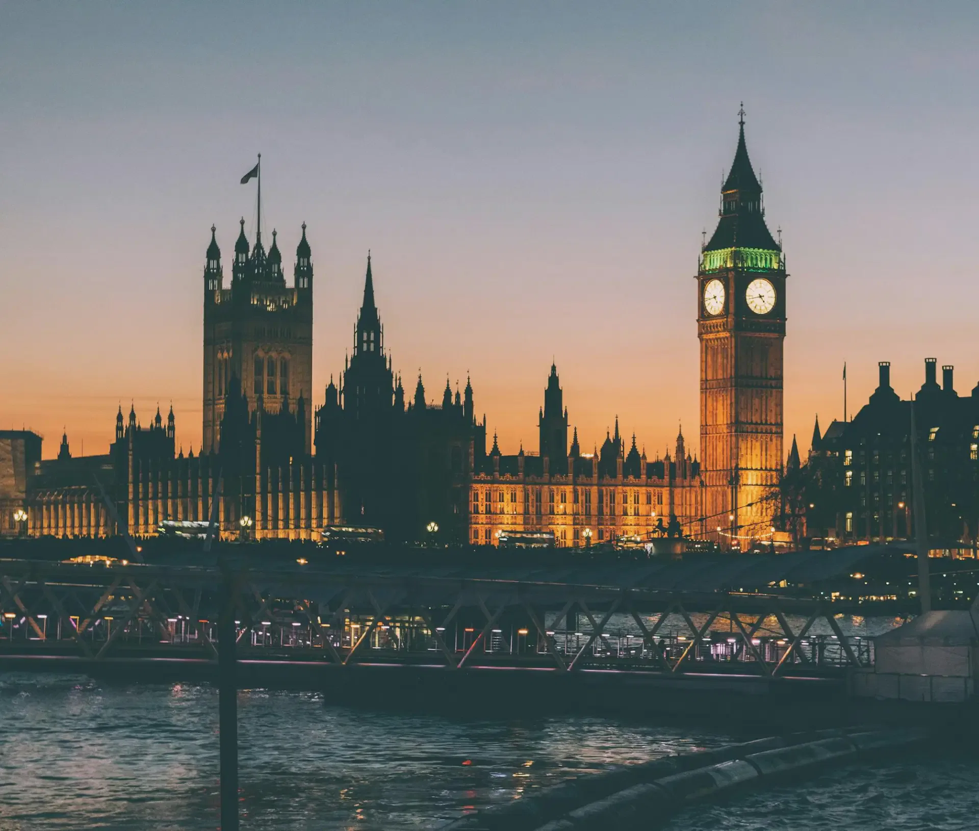 The Houses of Parliament and Big Ben in London are illuminated at sunset, with the Thames and Westminster Bridge in the foreground—a scene that any Apple Centric IT Partner or MSP would appreciate for its picturesque cityscape.