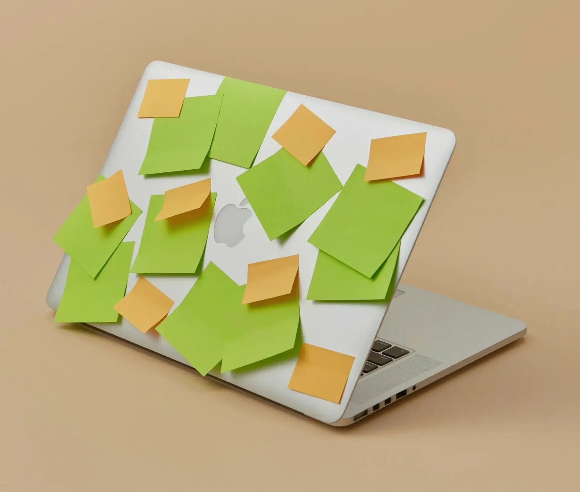 A silver laptop, partially open and covered in green and orange sticky notes, sits against a plain beige background—an essential tool for hybrid businesses shaping their IT strategy.