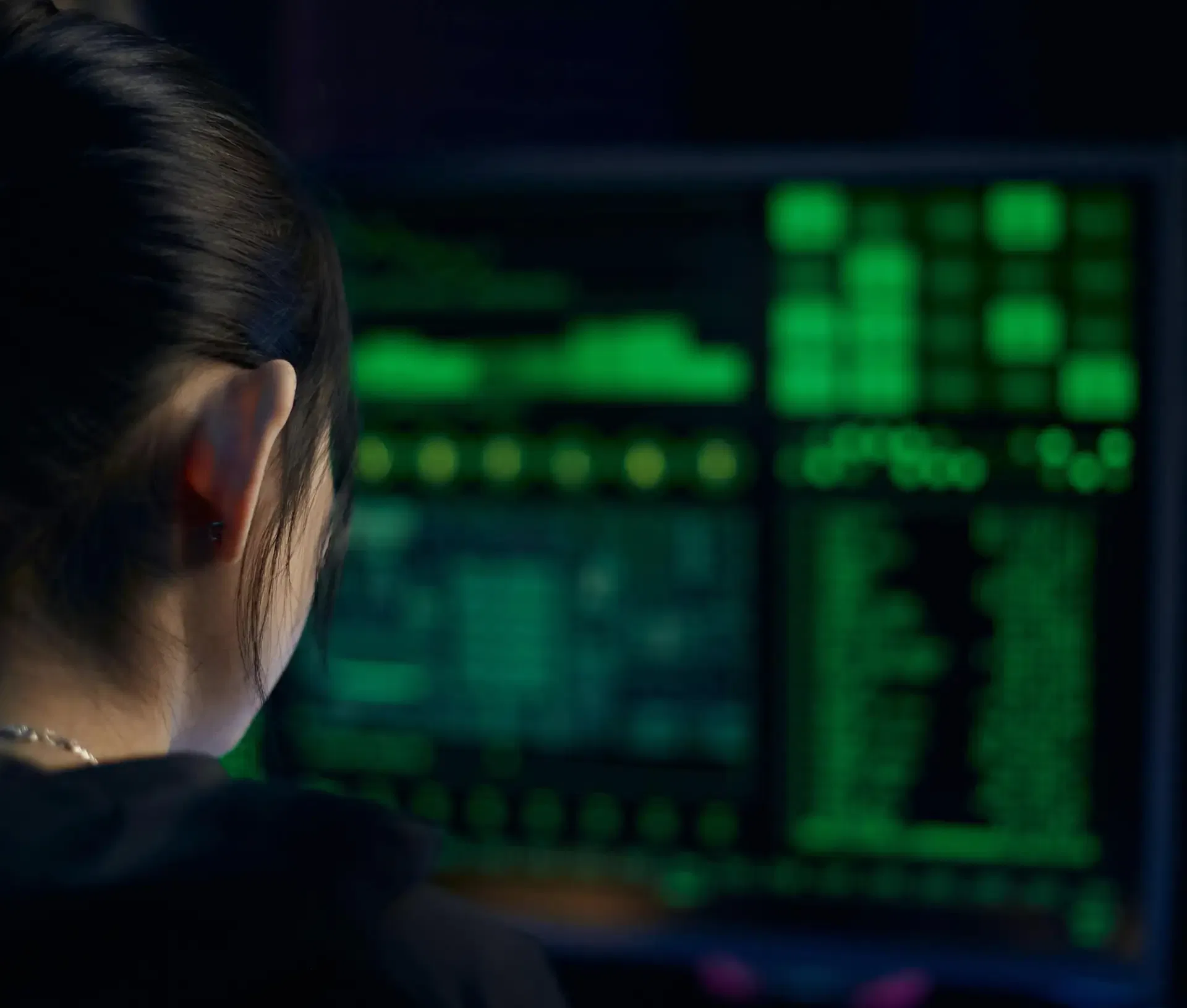 A person with dark hair, seen from behind, looks at a computer screen displaying green code and data on a dark background, suggesting cyber security activity or trend analysis for 2026.