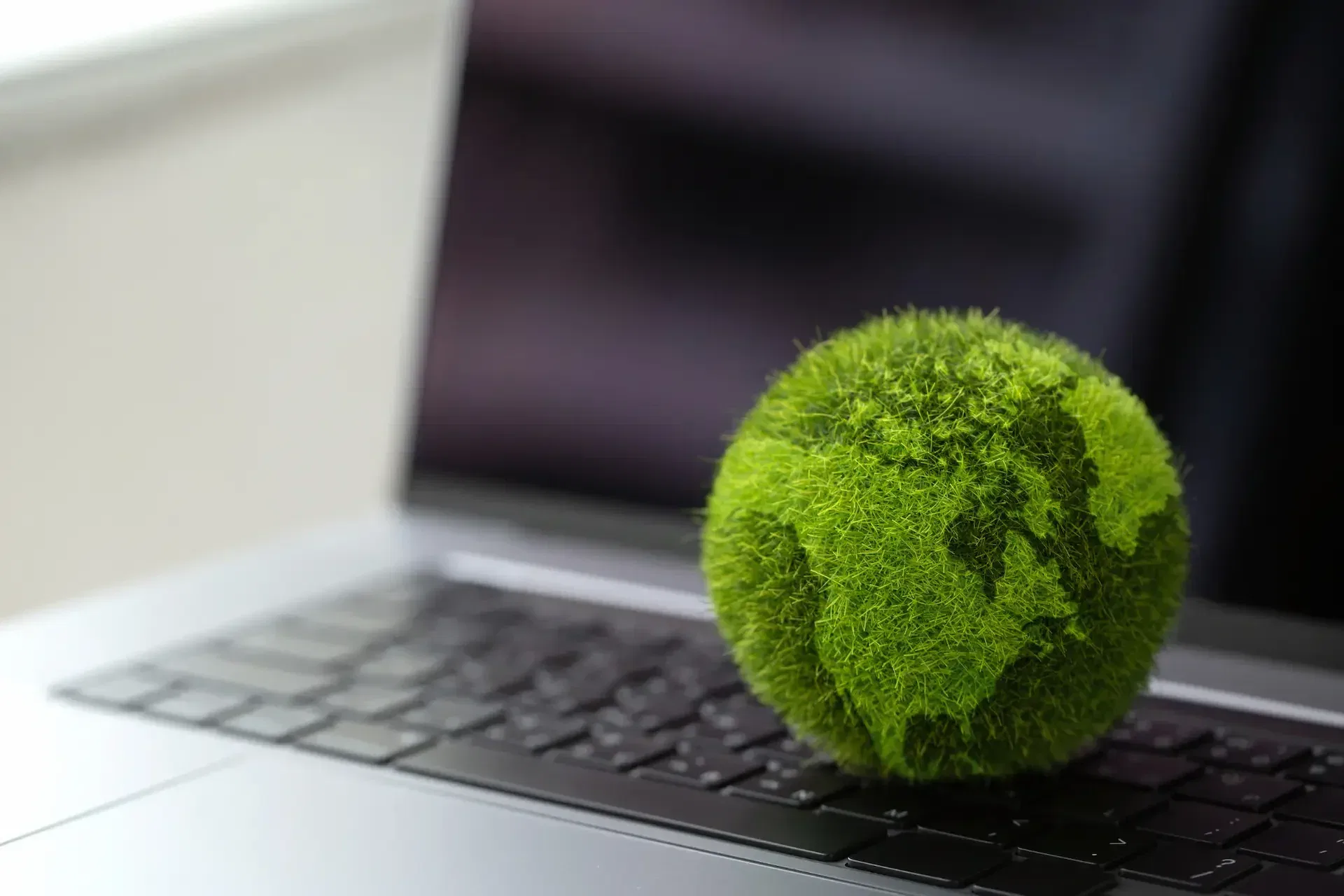 A small green globe covered in grass like texture sits on the keyboard of an open laptop, symbolizing smarter choices for a greener planet through it greener solutions.