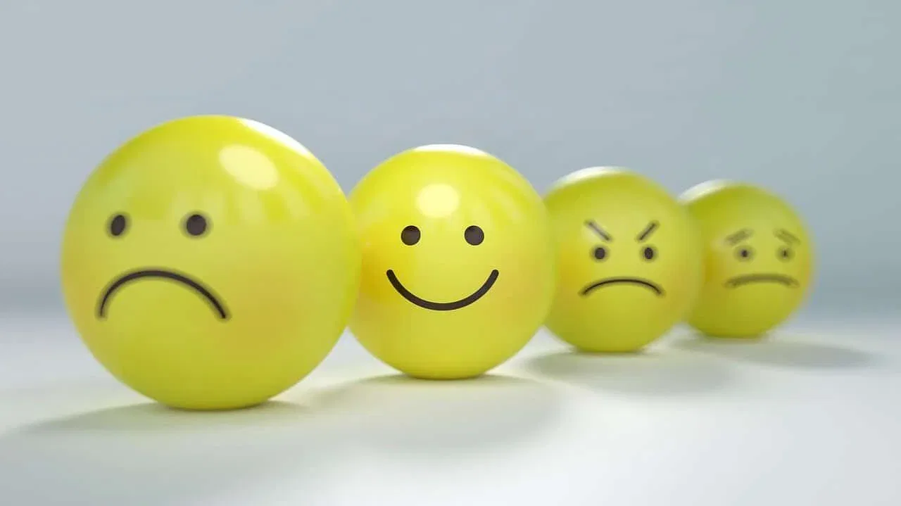 Four yellow spheres with drawn faces showing emotions—sad, happy, angry, and confused—are arranged in a line, perfectly capturing how teams might feel during a change it provider transition.