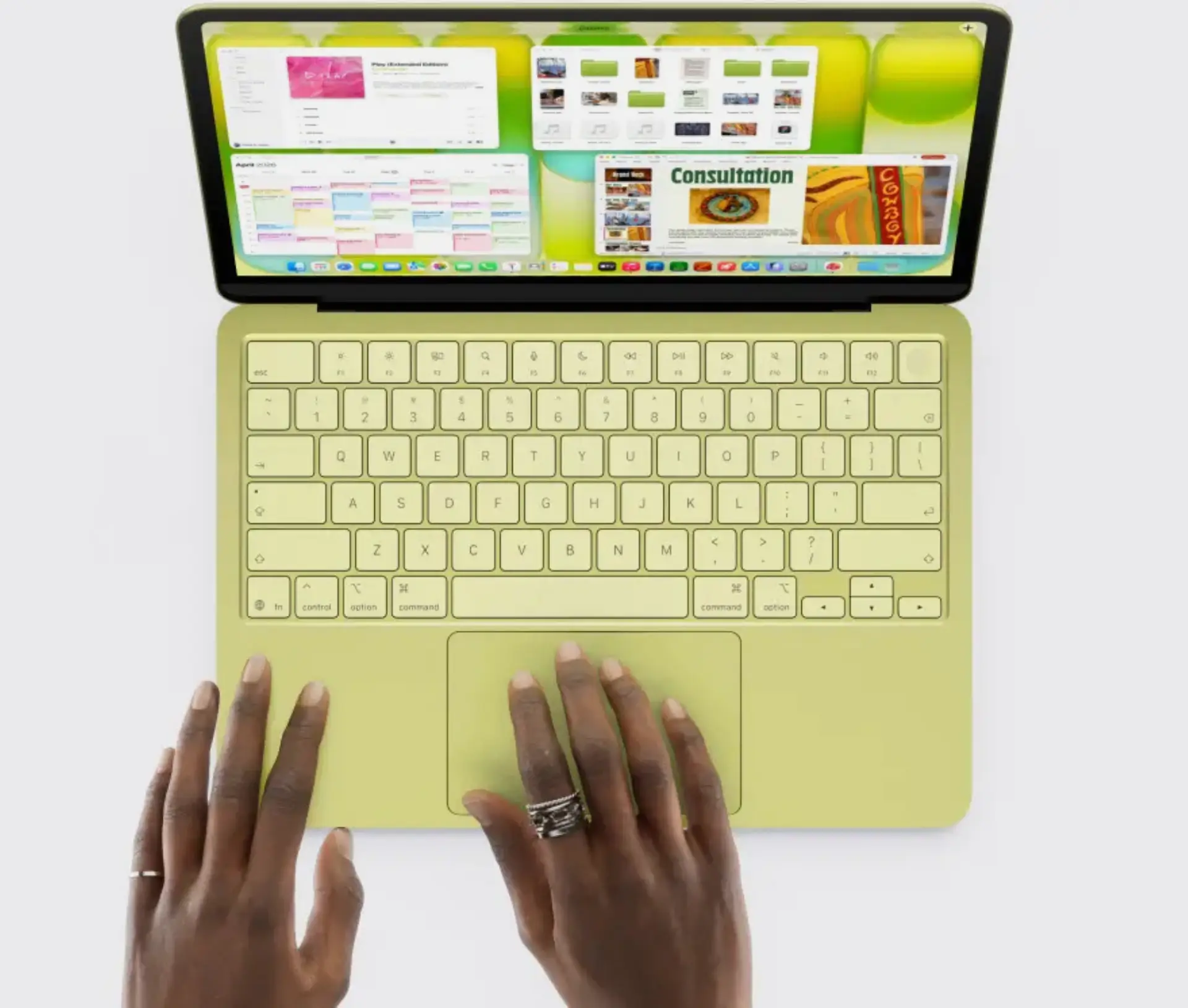 A person with rings on their fingers types on a yellow laptop, reminiscent of the £599 Mac or MacBook Neo, its large screen displaying multiple open windows and colourful apps. The view from above shows both hands at work, capturing the new wave of switchers in action.