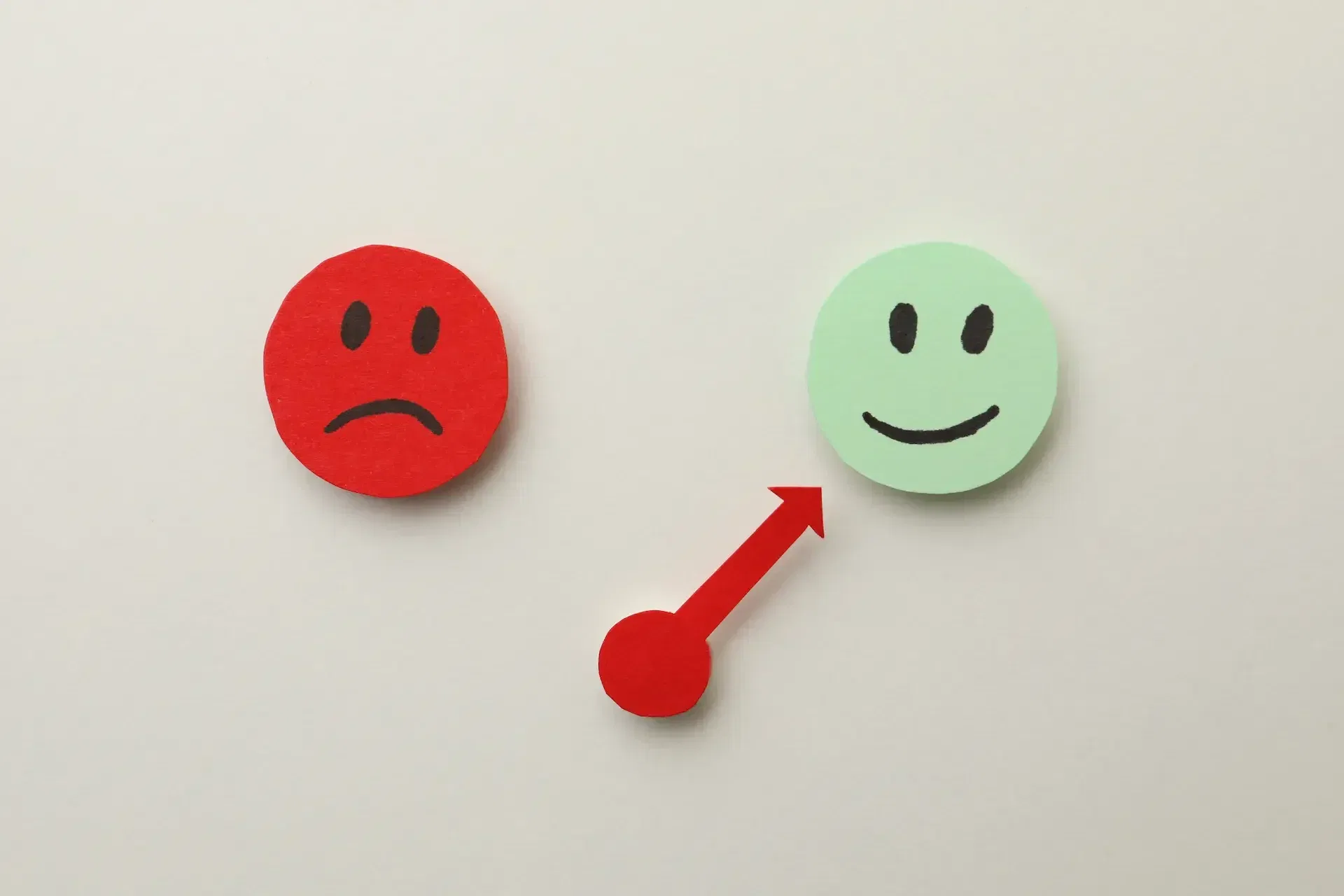 A red sad face transitions to a green happy face, connected by a red arrow pointing from left to right—illustrating how tech teams can improve mental health by working smarter.