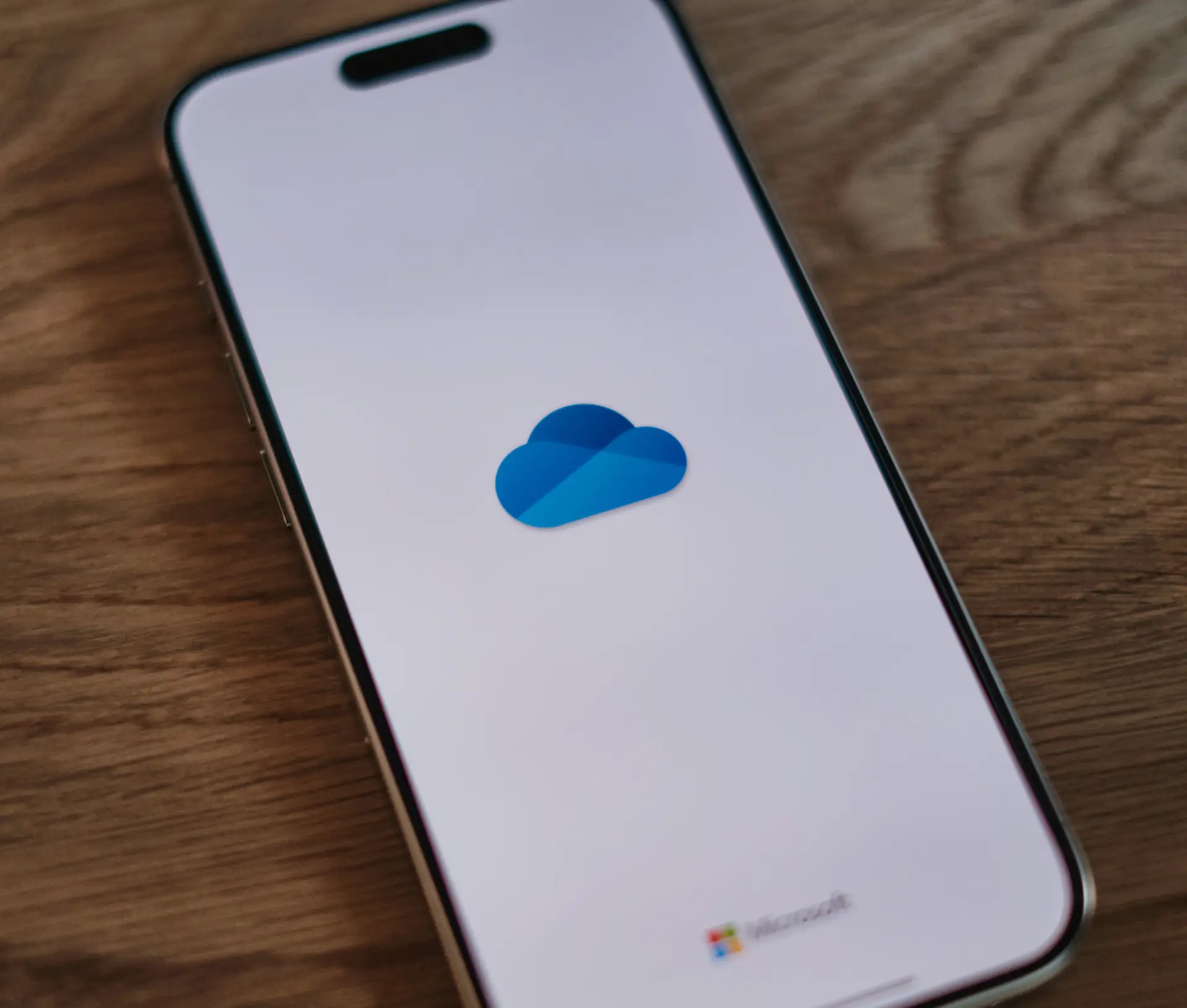 A smartphone displaying the Microsoft OneDrive cloud logo on its screen, resting on a wooden surface—highlighting the latest May Update that enhances how deleted files are managed.