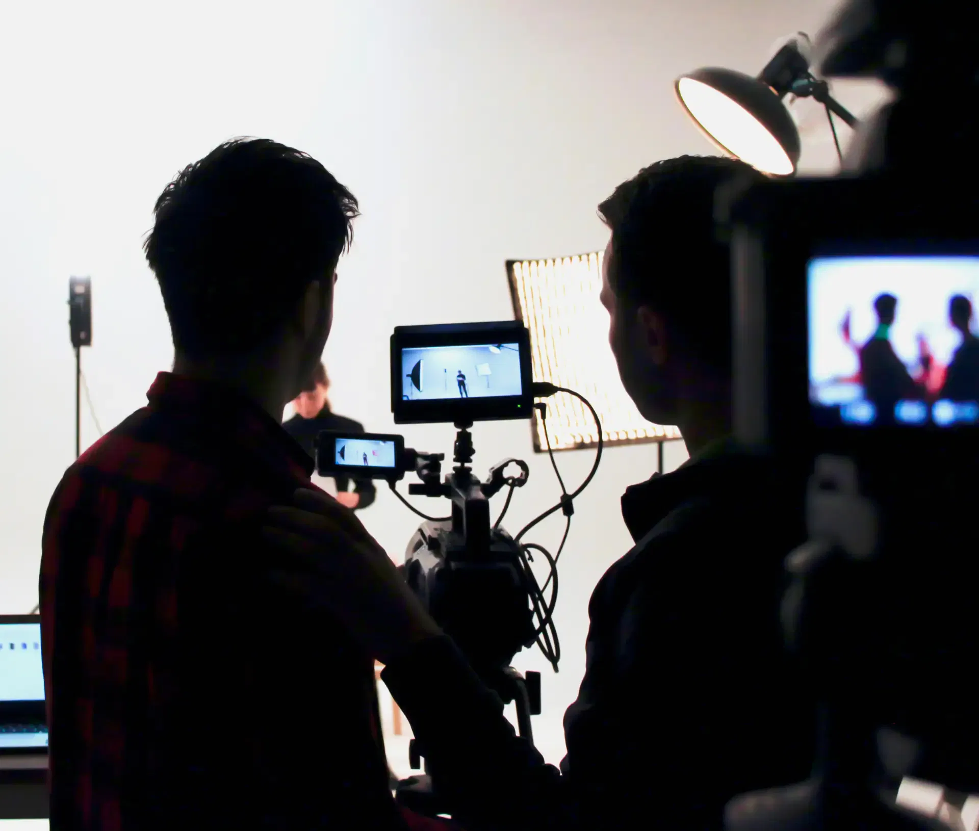 Two people operate a professional video camera and monitor in a brightly lit studio, filming a person against a white backdrop—showcasing Security by Design principles crucial for FinTech promotional content.