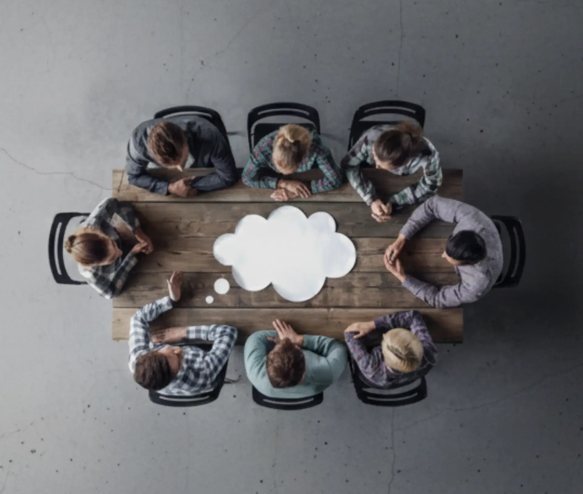 Seven people sit around a wooden table seen from above, with a white thought bubble in the centre, suggesting a brainstorming session focused on business benefits within the evolving UK AI landscape.
