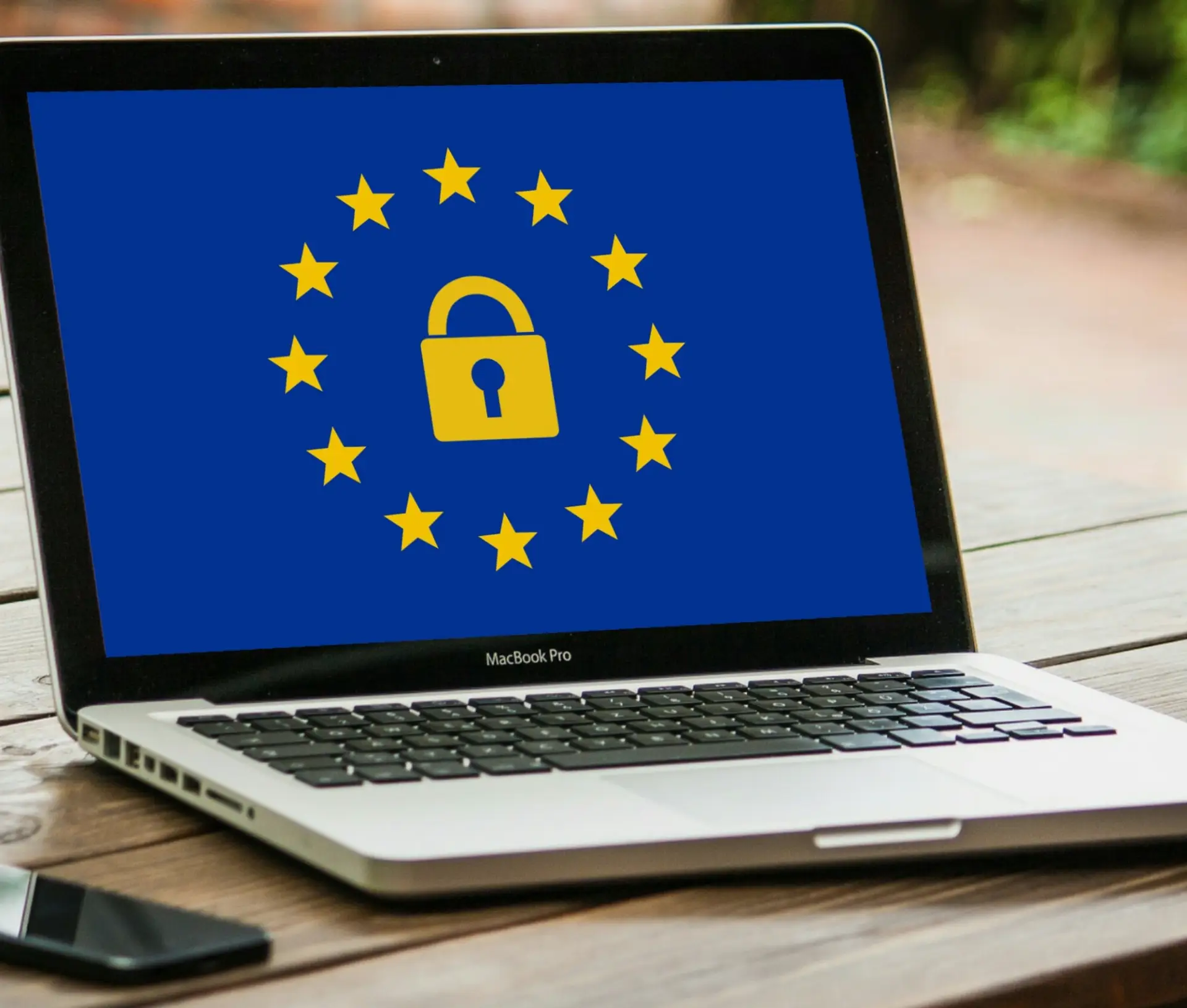 A laptop displays a blue screen with a yellow padlock surrounded by twelve yellow stars in a circle, symbolising the European Union and data protection, likely referencing GDPR privacy compliance.
